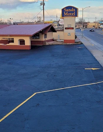 A retro roadside motel with a blue parking lot, beige and brown building, and a Sands Motel sign in the distance.