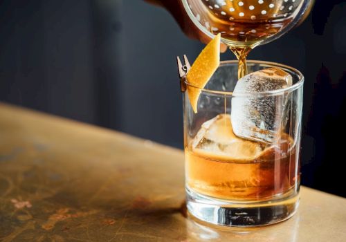 A glass of whiskey on the rocks with a garnish, being poured from a bottle.