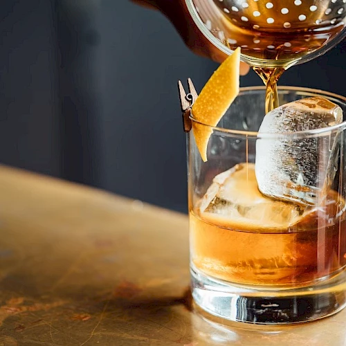 A glass of whiskey on the rocks with a garnish, being poured from a bottle.