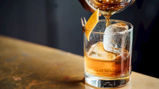 A glass of whiskey on the rocks with a garnish, being poured from a bottle.