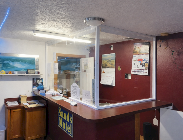 A compact, modern kitchen with a red accent wall, wooden island, white appliances, and a window bringing natural light.